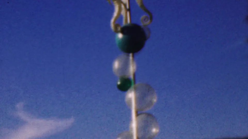 The camera frames the hanging sea horse motif and vertical string of green and clear glass bubbles from below, set against the bright sky at the 1964 Anaheim Disneyland location described in metadata.