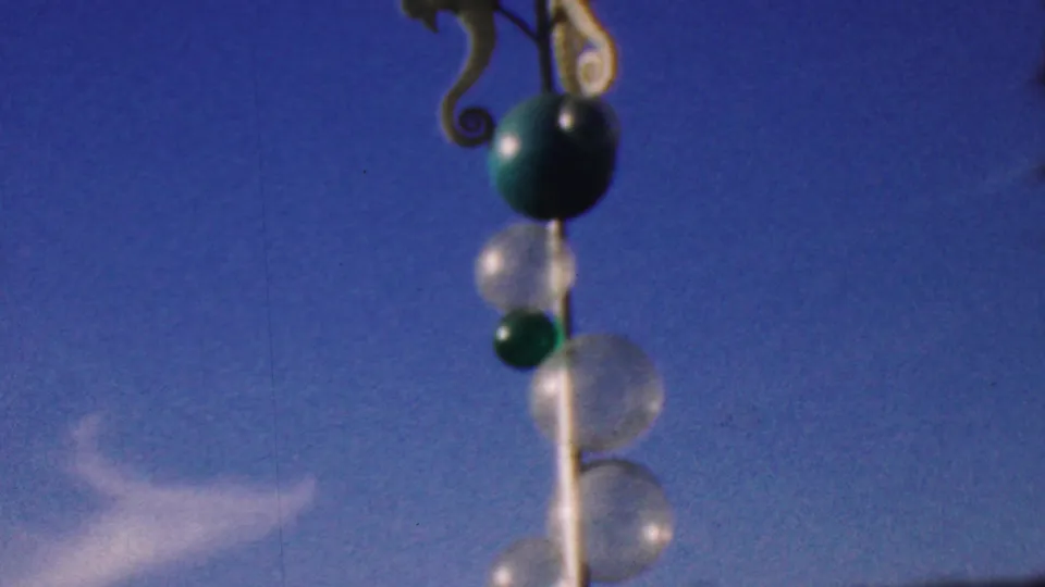 Later frame of the visitor-shot sculpture detail, showing the sea horse ornament, green orb, clear bubbles, and white support isolated against the blue sky in the 1964 Anaheim Disneyland footage.