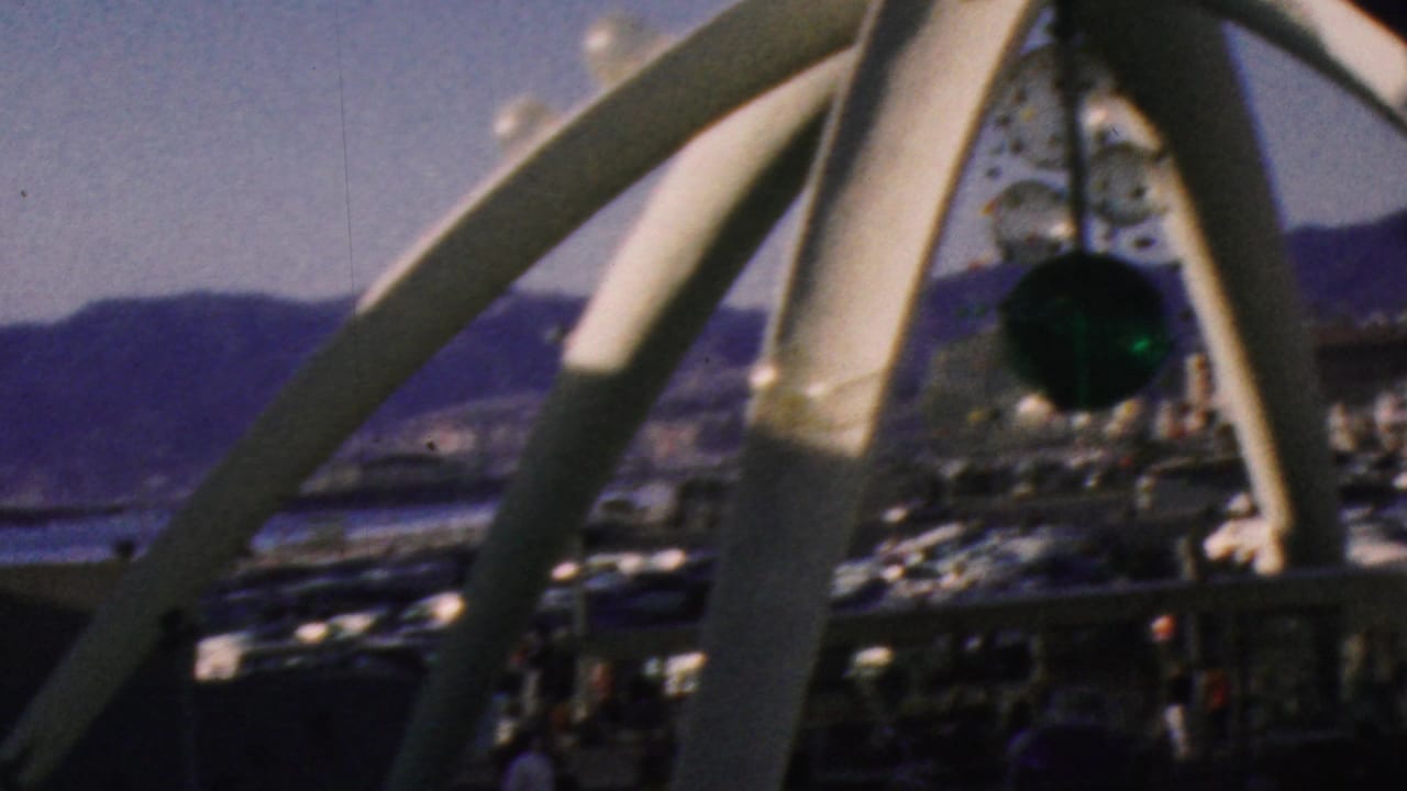 1964 Anaheim theme-park frame showing white curved supports in the foreground with water, distant mountains, and darker attraction structures beyond.