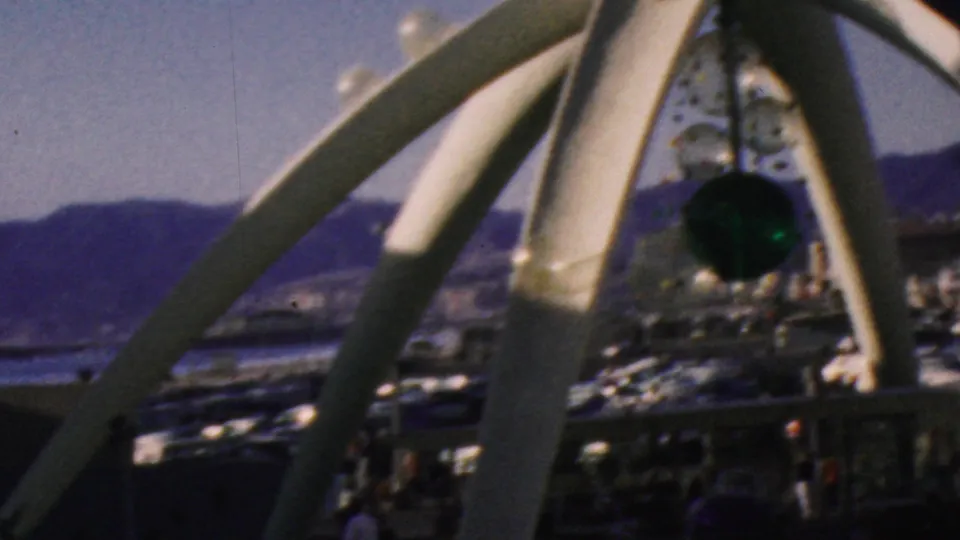 1964 Anaheim theme-park frame showing white curved supports in the foreground with water, distant mountains, and darker attraction structures beyond.