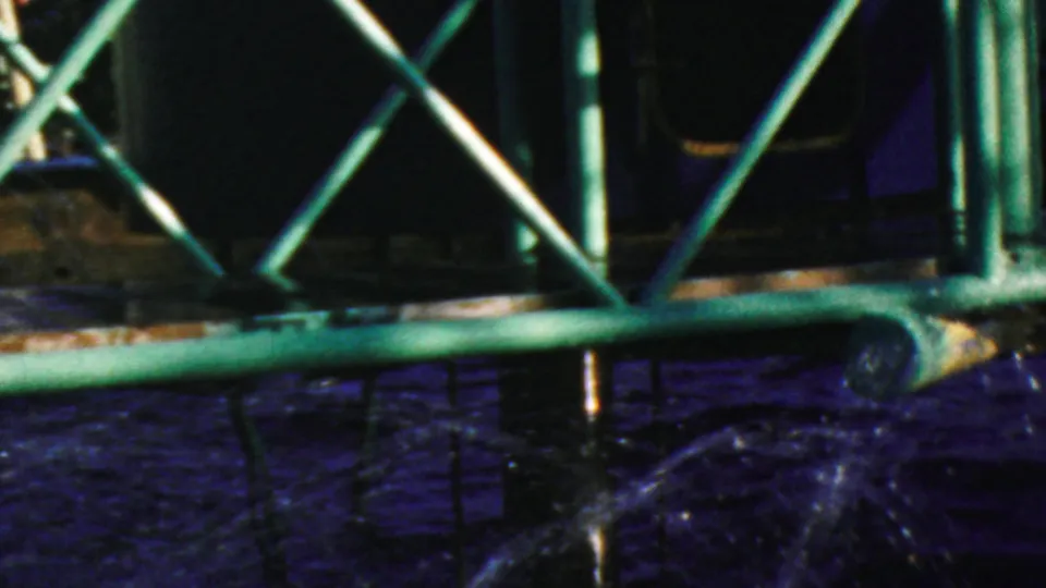 Close 1964 Anaheim Disneyland view of a dark submarine-like ride structure behind green railings, with water splashing below and portholes visible in shadow.