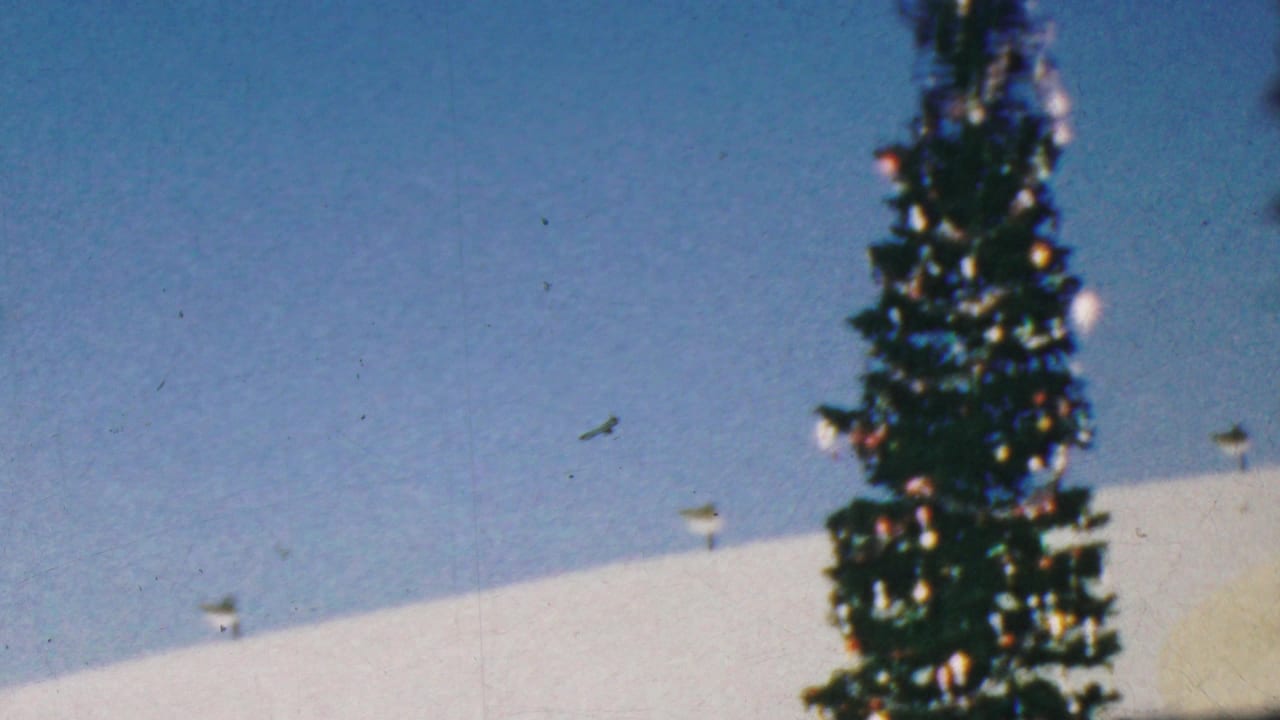 1964 Anaheim Disneyland frame with the upper portion of a decorated Christmas tree, pale snow-like structure, and small roofline details in bright daylight.