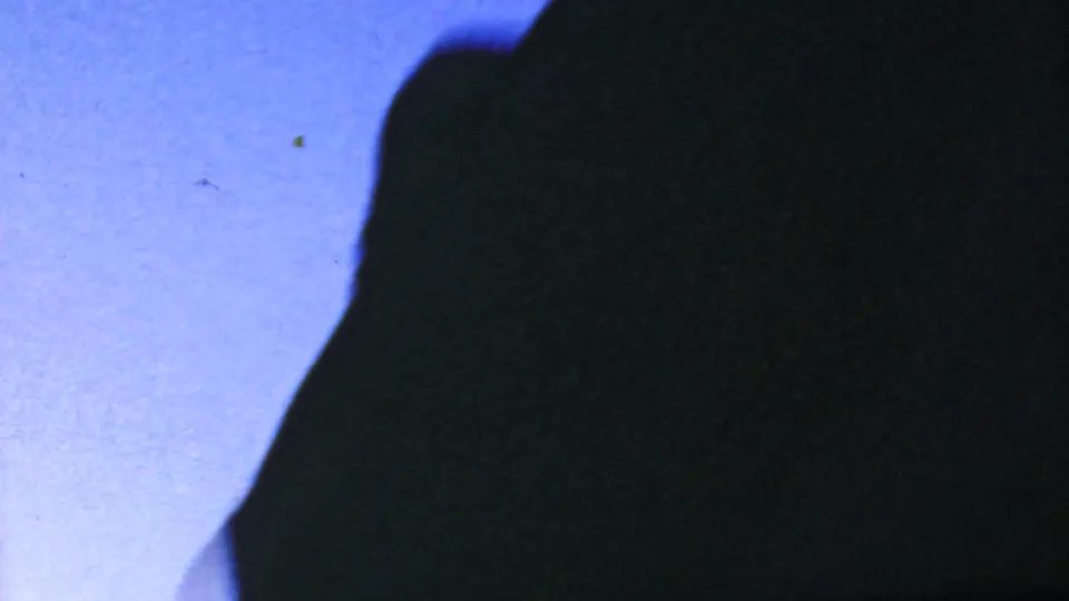 A dark, close silhouette or shadowed surface dominates the frame, with a strip of blue sky at left and visible 8mm grain from the 1964 Anaheim home movie.
