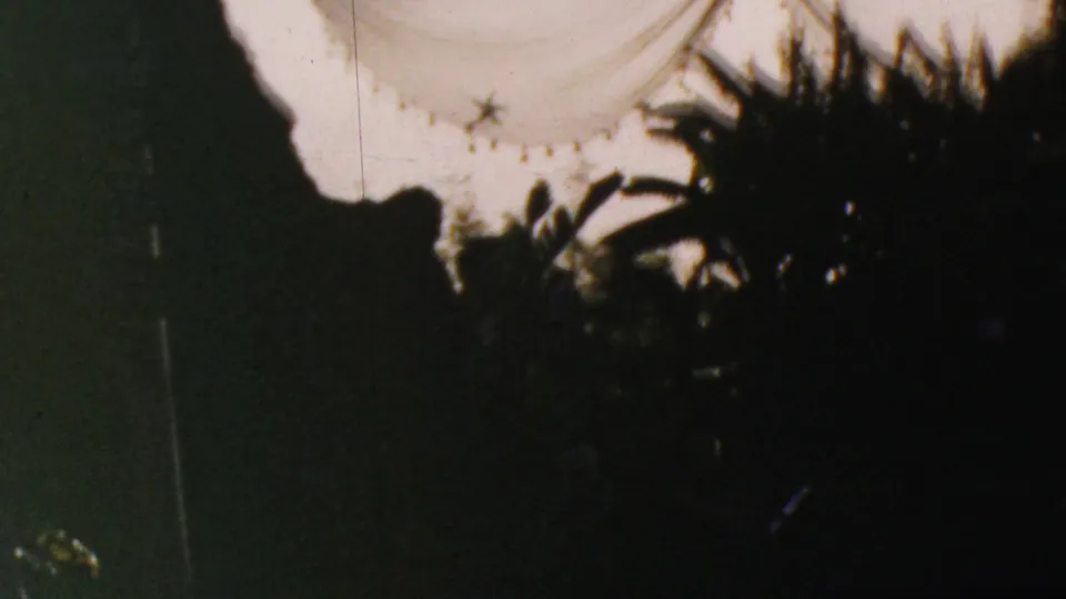 1964 Anaheim home-movie frame with the right edge of the Mystery Island sign, a dark rock or mountain-like silhouette, and silhouetted foliage against a pale sky.