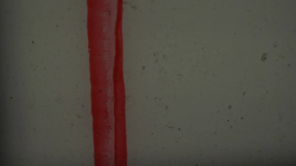 Close-up of a red stamped vertical mark with a rounded lower end on a pale textured surface, from supplied 1965 Los Angeles 8mm footage.