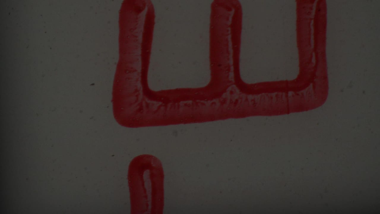 Partial red rectangular stamp shape with vertical indentations and a separate red ink line on a pale surface in supplied 1965 8mm footage.