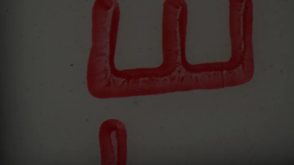 Partial red rectangular stamp shape with vertical indentations and a separate red ink line on a pale surface in supplied 1965 8mm footage.