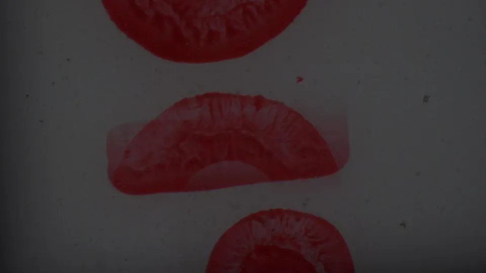 Close-up of two curved red ink stamp fragments on a pale textured surface, consistent with the supplied 1965 8mm home-movie material.