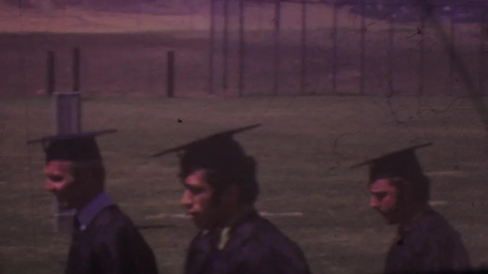 Graduates in black mortarboards and gowns process across an outdoor school field during the Los Angeles graduation ceremony.