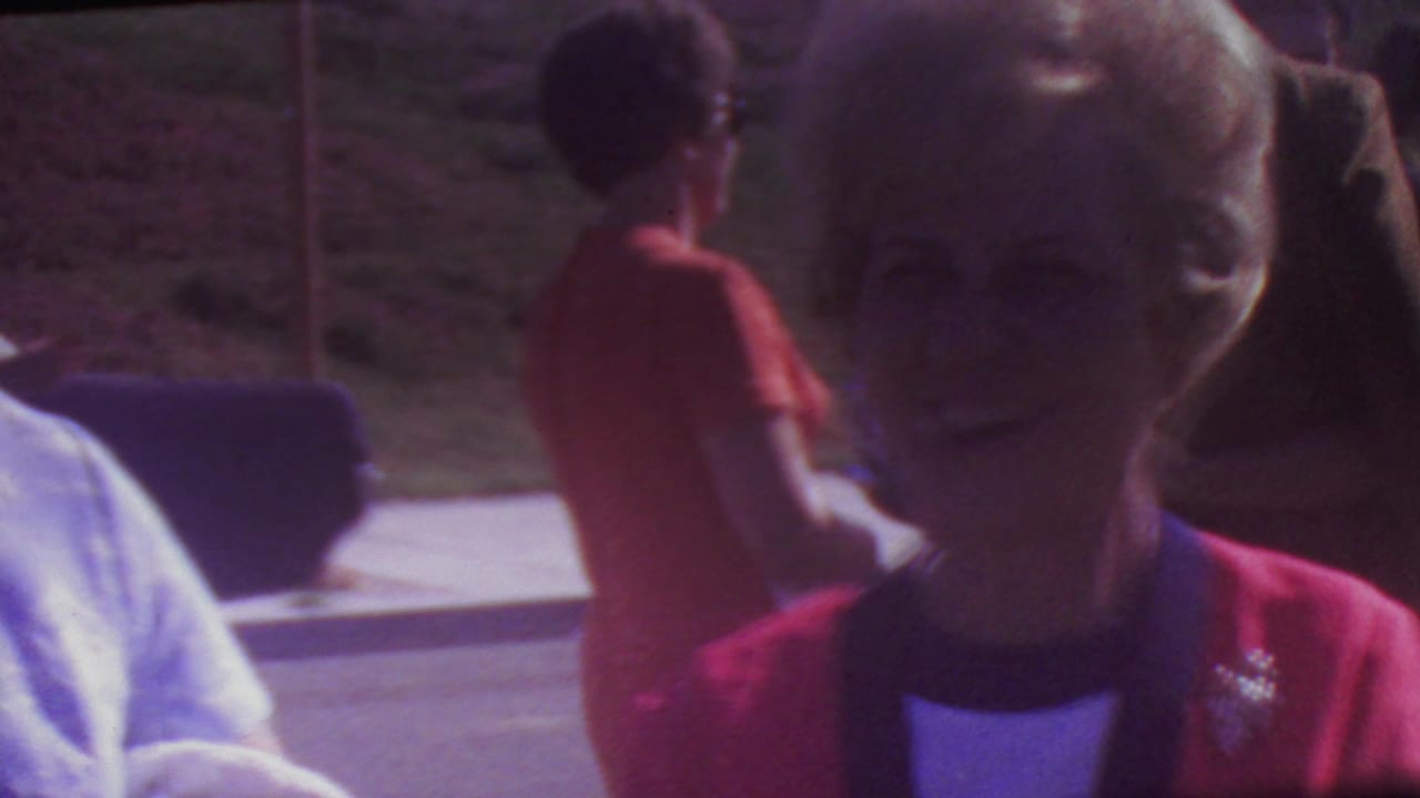 Woman in a red jacket smiling near the camera while another person stands behind her outdoors.