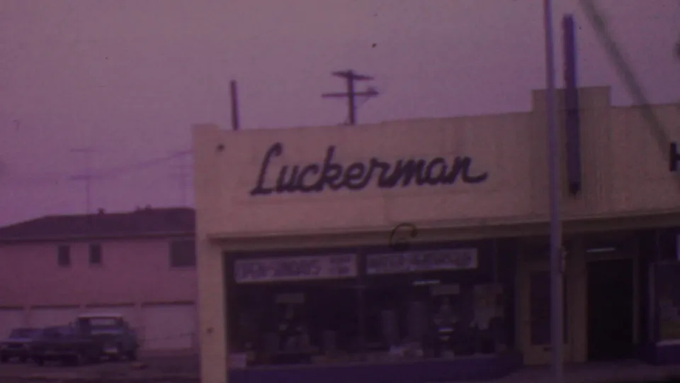The final frame holds on the Luckerman storefront in Los Angeles with display windows, a dark doorway, utility wires, and cars parked along the street.