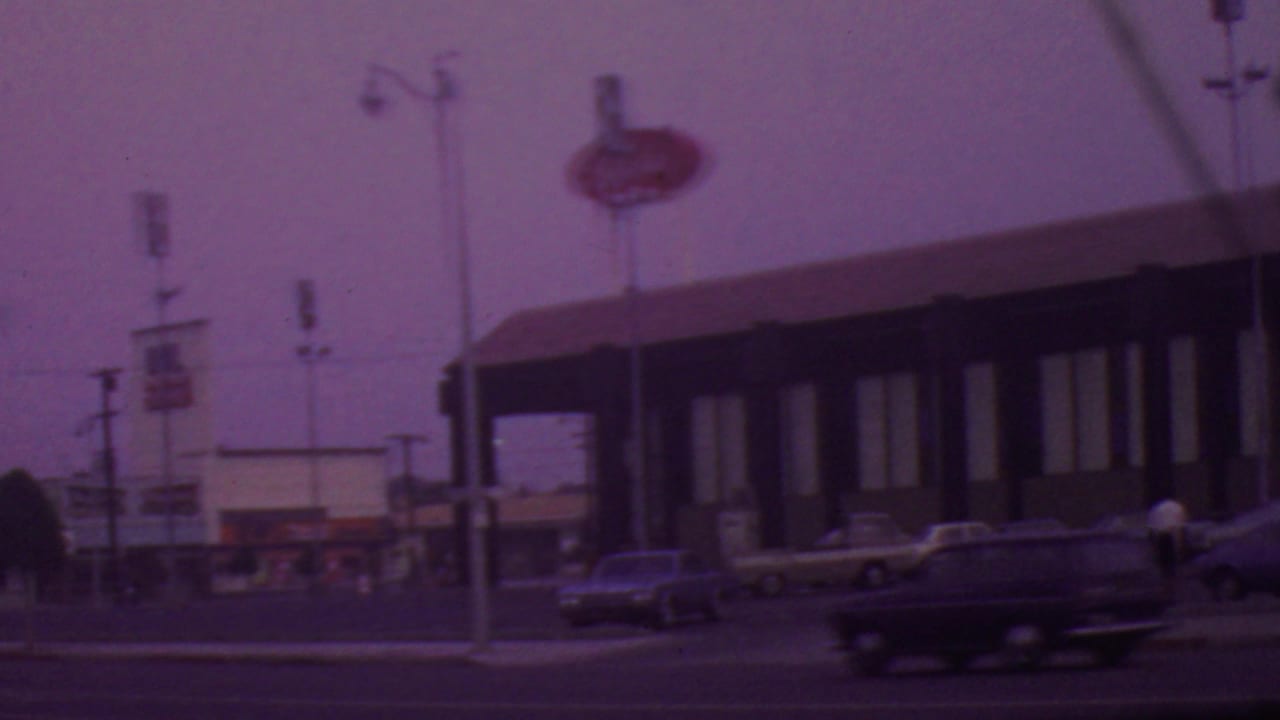 Wider street view with restaurant sign, parked cars, traffic, and a pedestrian.