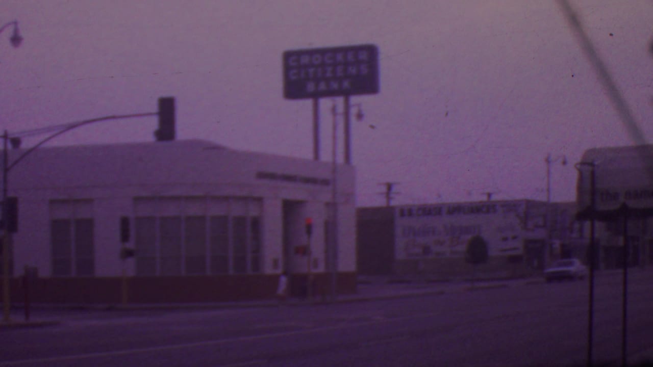 1965 Los Angeles street view with a Crocker Citizens Bank sign above a low commercial building, traffic signals, a billboard, and cars in the distance.