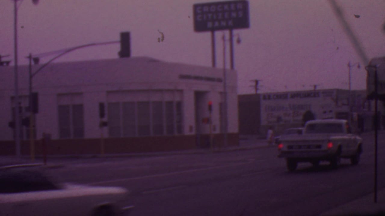 A classic pickup truck drives through a Los Angeles intersection near the Crocker Citizens Bank building, traffic lights, and a B.B. Chase Appliances billboard.