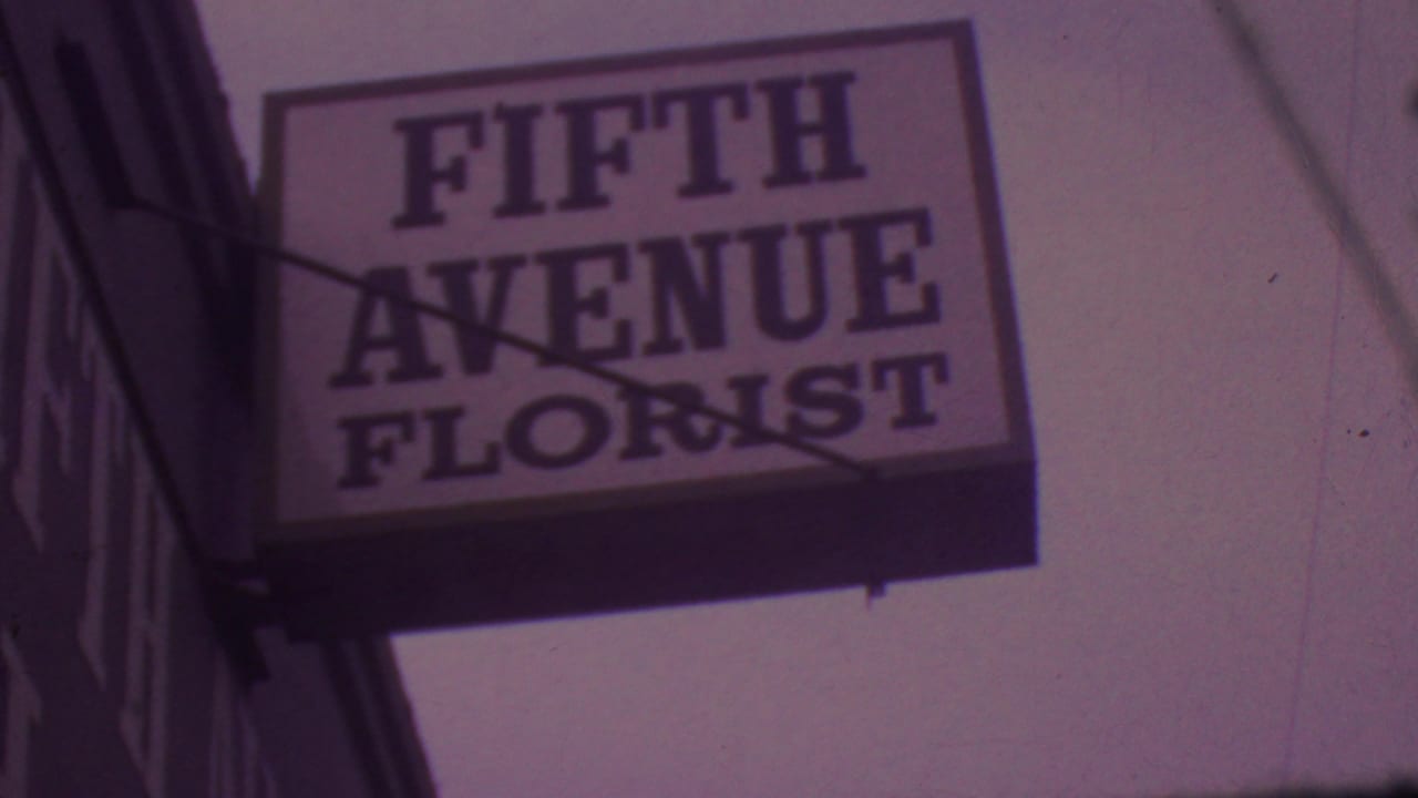 Close view of the Fifth Avenue Florist sign in 1965 Los Angeles footage, framed from below with visible sign supports and soft film grain.