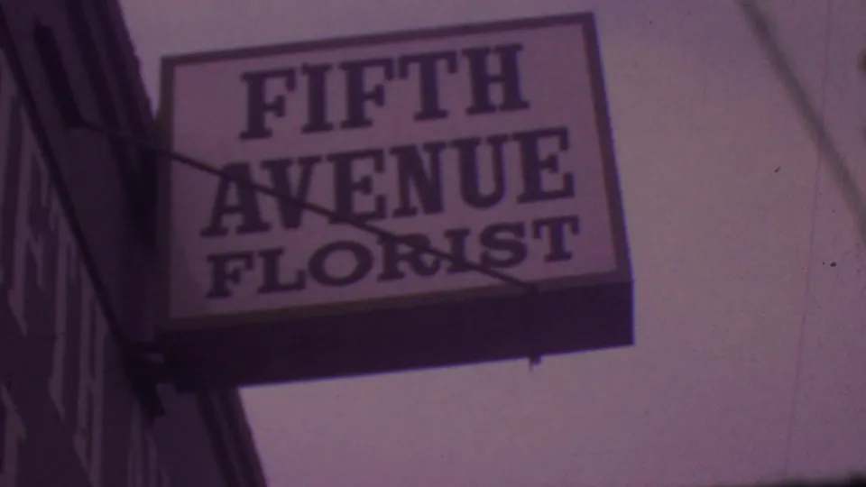 Close view of the Fifth Avenue Florist sign in 1965 Los Angeles footage, framed from below with visible sign supports and soft film grain.