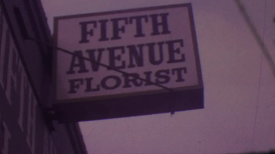 1965 Los Angeles 8mm frame showing a low-angle view of a rectangular Fifth Avenue Florist sign with bold lettering and shadowed support rods.