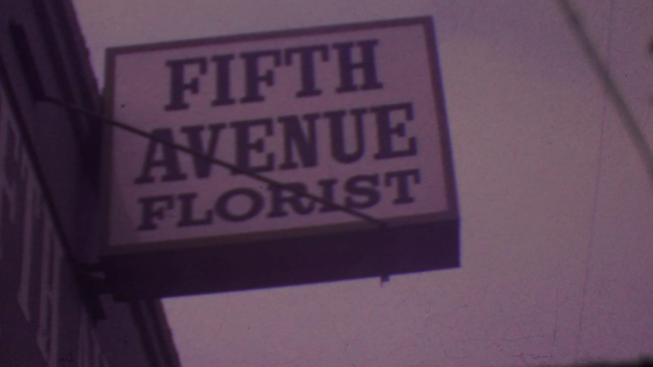 Projecting Fifth Avenue Florist sign framed from below with the building edge at left.