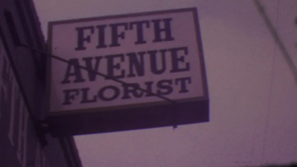 1965 Los Angeles frame with the Fifth Avenue Florist sign filling the upper view, filmed from a low sidewalk angle with soft 8mm grain.
