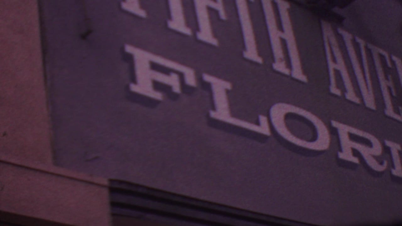 1965 Los Angeles frame showing a tight, angled crop of the Fifth Avenue Florist wall signage, with large raised-looking letters and visible film grain.