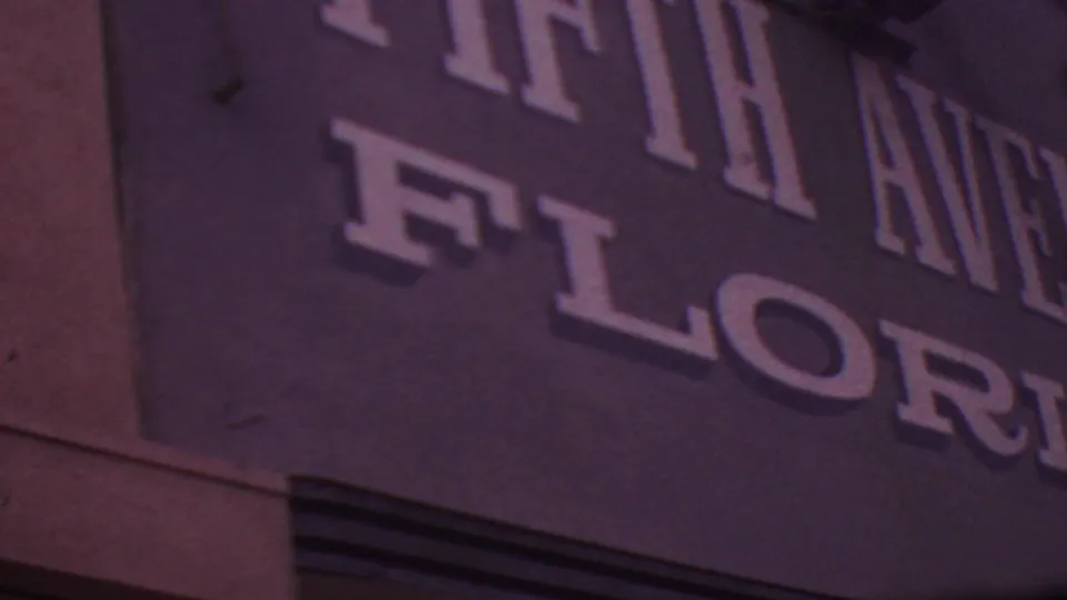 1965 Los Angeles frame showing a tight, angled crop of the Fifth Avenue Florist wall signage, with large raised-looking letters and visible film grain.