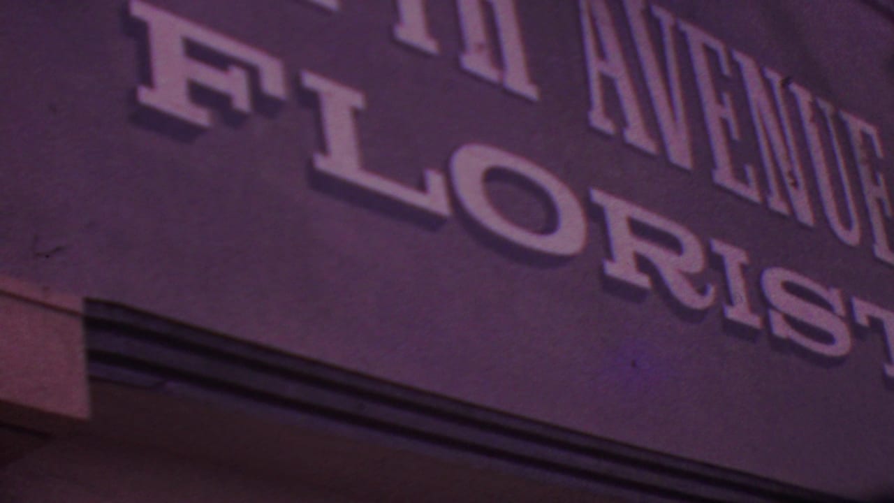 Tight 8mm frame of the Fifth Avenue Florist storefront sign in Los Angeles, showing raised lettering and the dark textured sign panel.