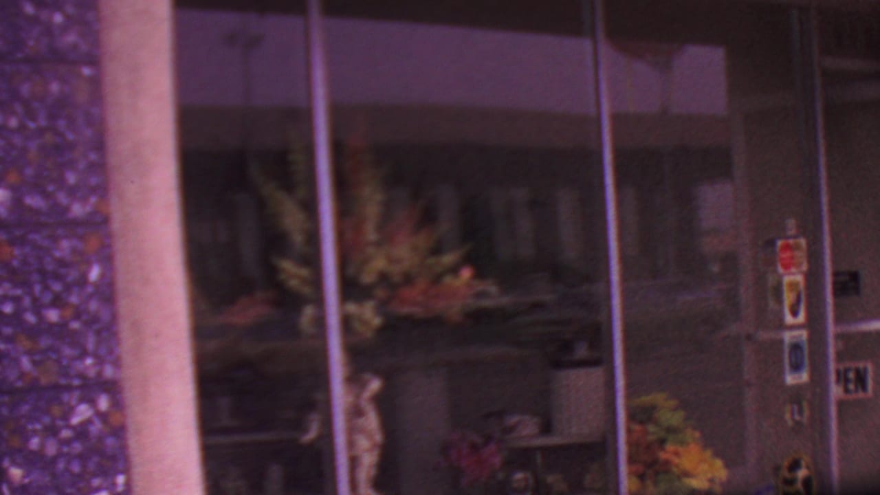 Glass florist storefront with arrangements visible inside and stickers on the door.