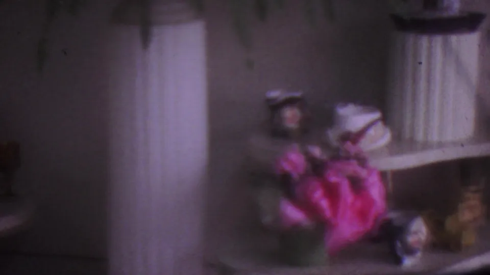 1965 Los Angeles home interior frame showing a low display table with pink-wrapped flowers, small figurines, and a tall white planter.