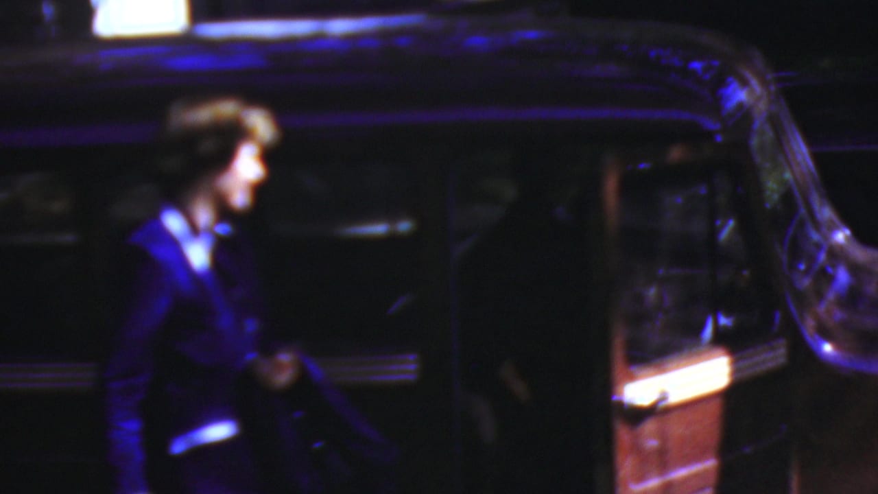 Woman in a dark coat stands next to a vintage car at night.