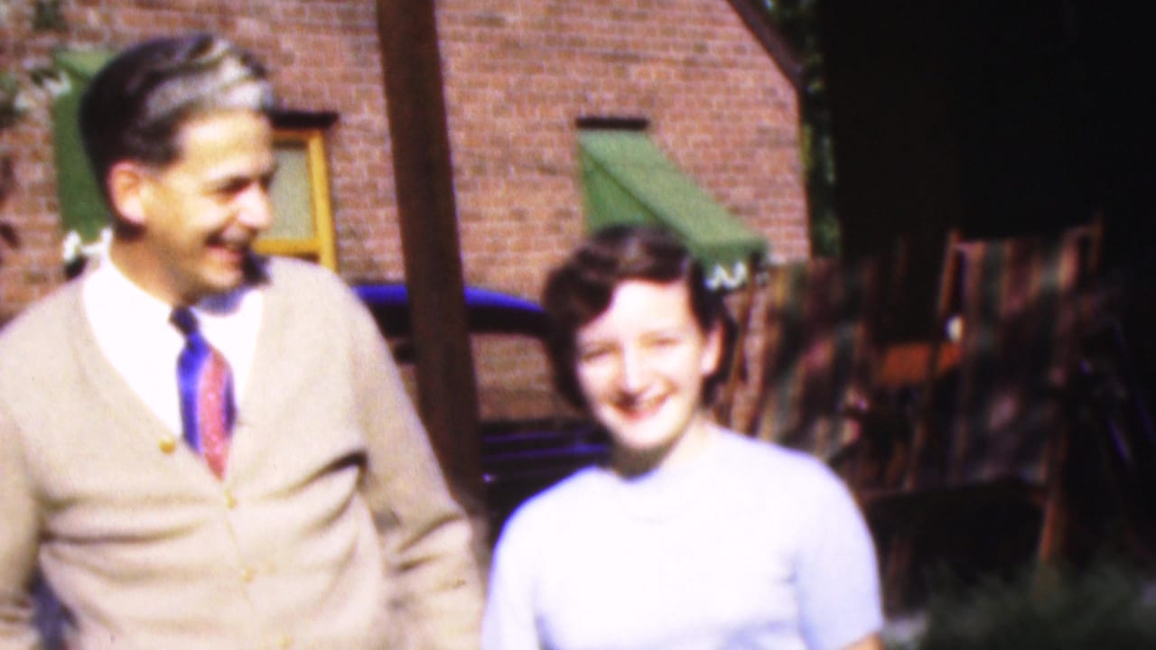Man looks toward a smiling woman beside a brick house and parked car.