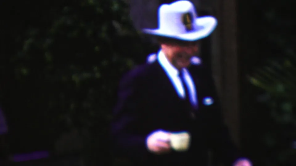 California 1961 home-movie frame showing a man in a white cowboy-style hat, dark suit, and tie walking outdoors with a white coffee cup.