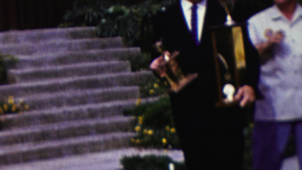 Adults stand on stone steps while suited men hold awards at the sides of the frame.