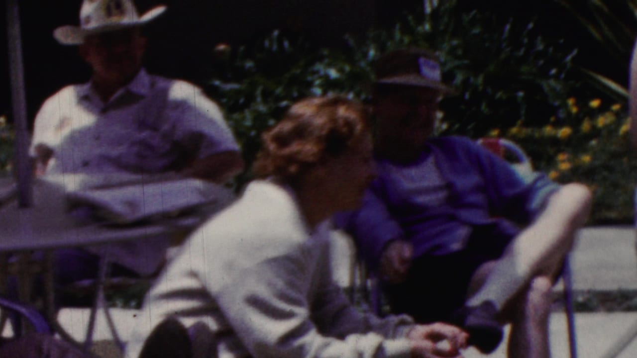 Adults sit outdoors around patio furniture in partial shade.