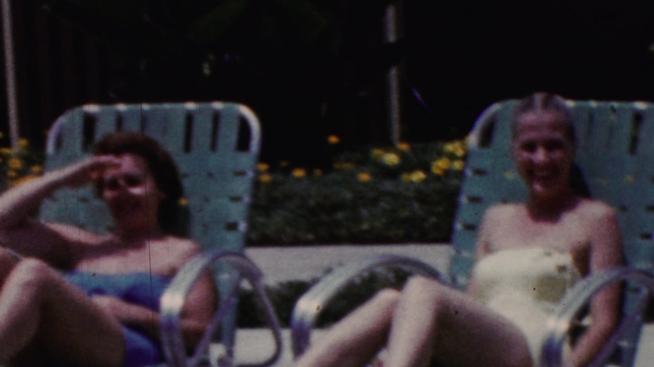 A woman in a blue swimsuit reclines on a turquoise lounge chair and shades her eyes from the sun.