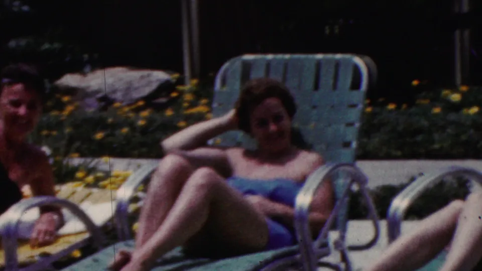 1961 California poolside home-movie frame showing a woman in a blue swimsuit reclining on a turquoise lounge chair, with another swimsuit-clad figure partly cropped at the side.