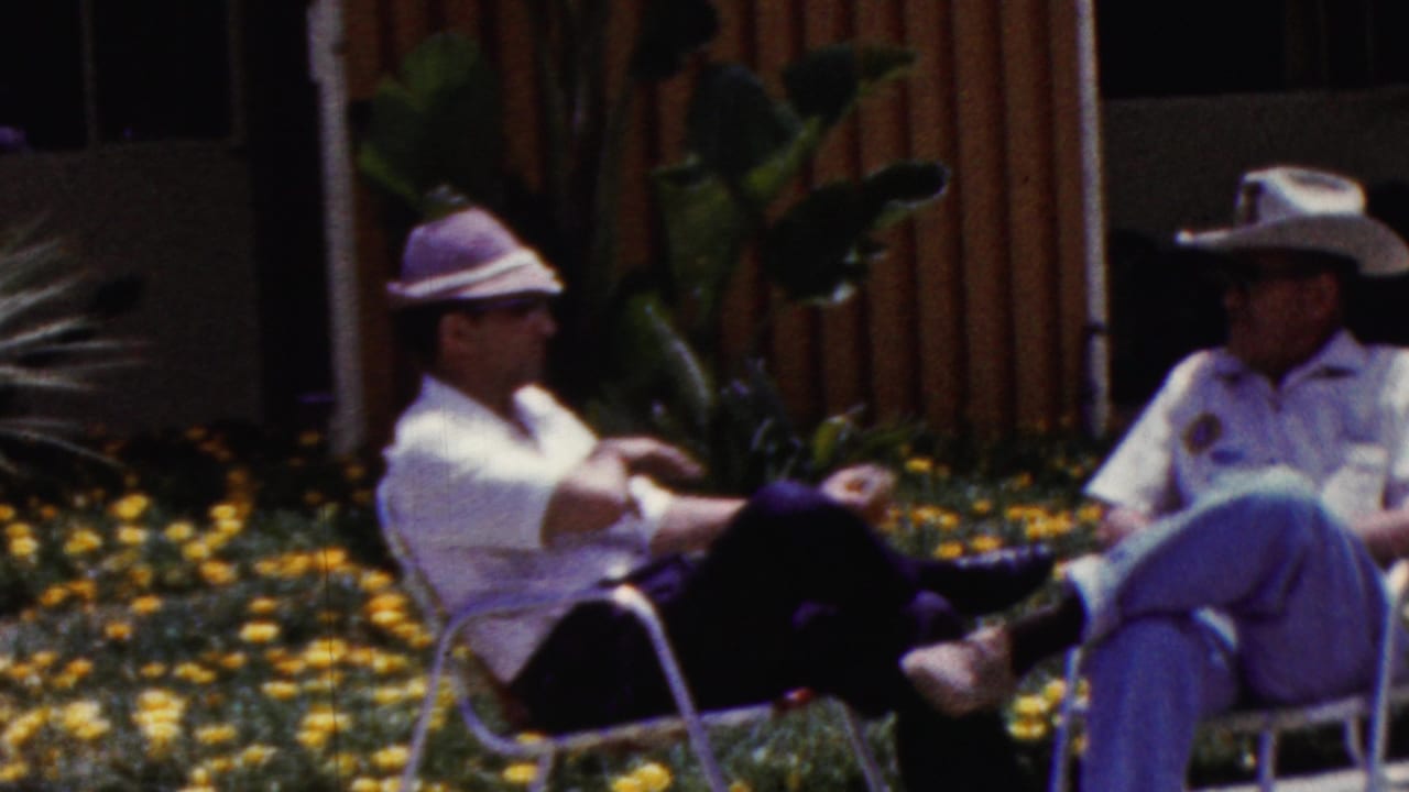 Two adults in broad hats sit facing each other on patio chairs.