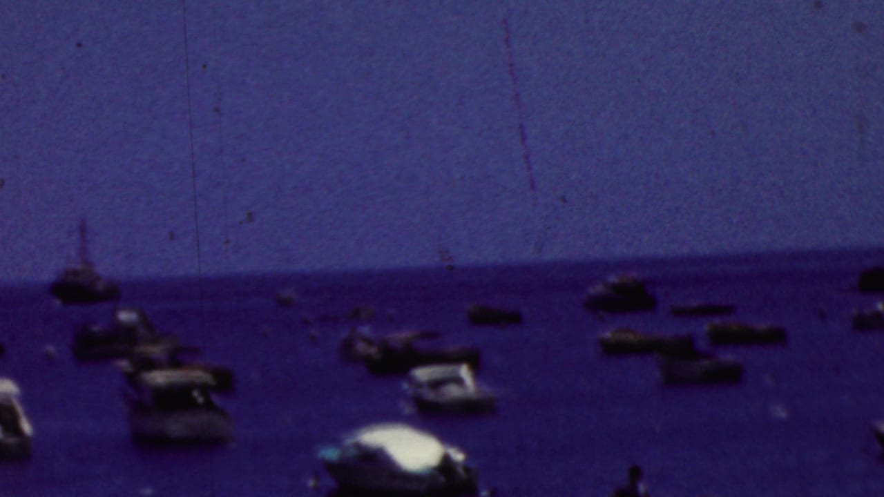 California 1961 8mm home-movie frame showing scattered small boats and motorboats on blue coastal water, viewed from a distant shoreline or overlook.
