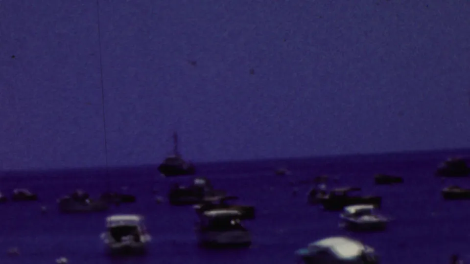 Distant small craft and motorboats sit across calm California coastal water in a soft, blue-shifted 1961 8mm frame.