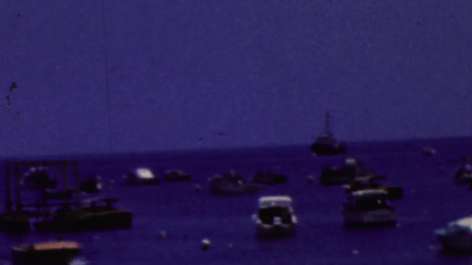 A 1961 California coastal home-movie view with boats near the foreground edge and additional small craft scattered across the water beyond.