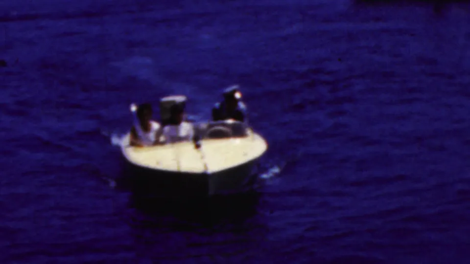 White-hulled motorboat on dark blue California coastal water with indistinct people aboard, captured in grainy 1961 8mm home-movie footage.