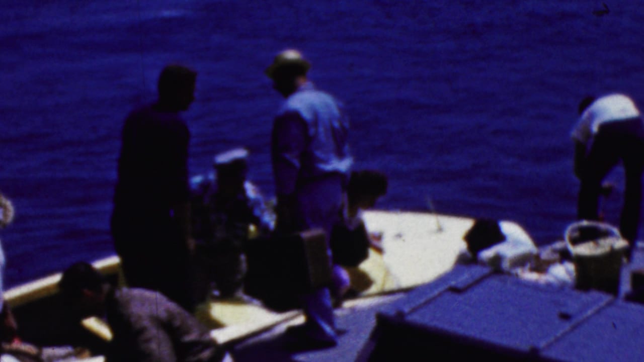 In supported 1961 California home-movie footage, several adults gather on a small boat deck with deep blue ocean filling the background.