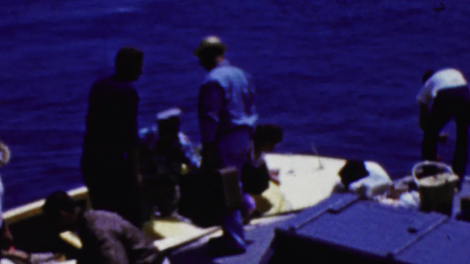 In supported 1961 California home-movie footage, several adults gather on a small boat deck with deep blue ocean filling the background.