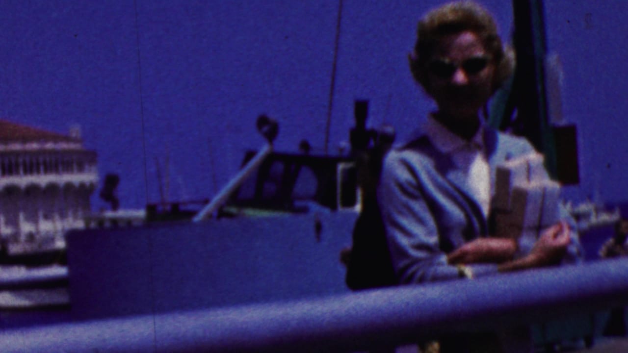 The woman remains on the boat deck in coastal California, partially shadowed by the exposure, with boat fittings, a railing, water, and a white building visible behind her.