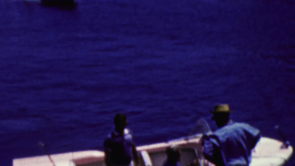The camera looks across blue harbor water toward a small boat carrying passengers, continuing the 1961 California recreational boating scene.