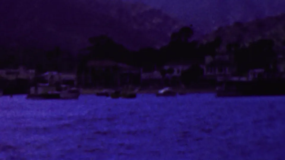 A soft 8mm view across dark blue water toward a California shoreline with houses, trees, and several small boats visible in the distance.
