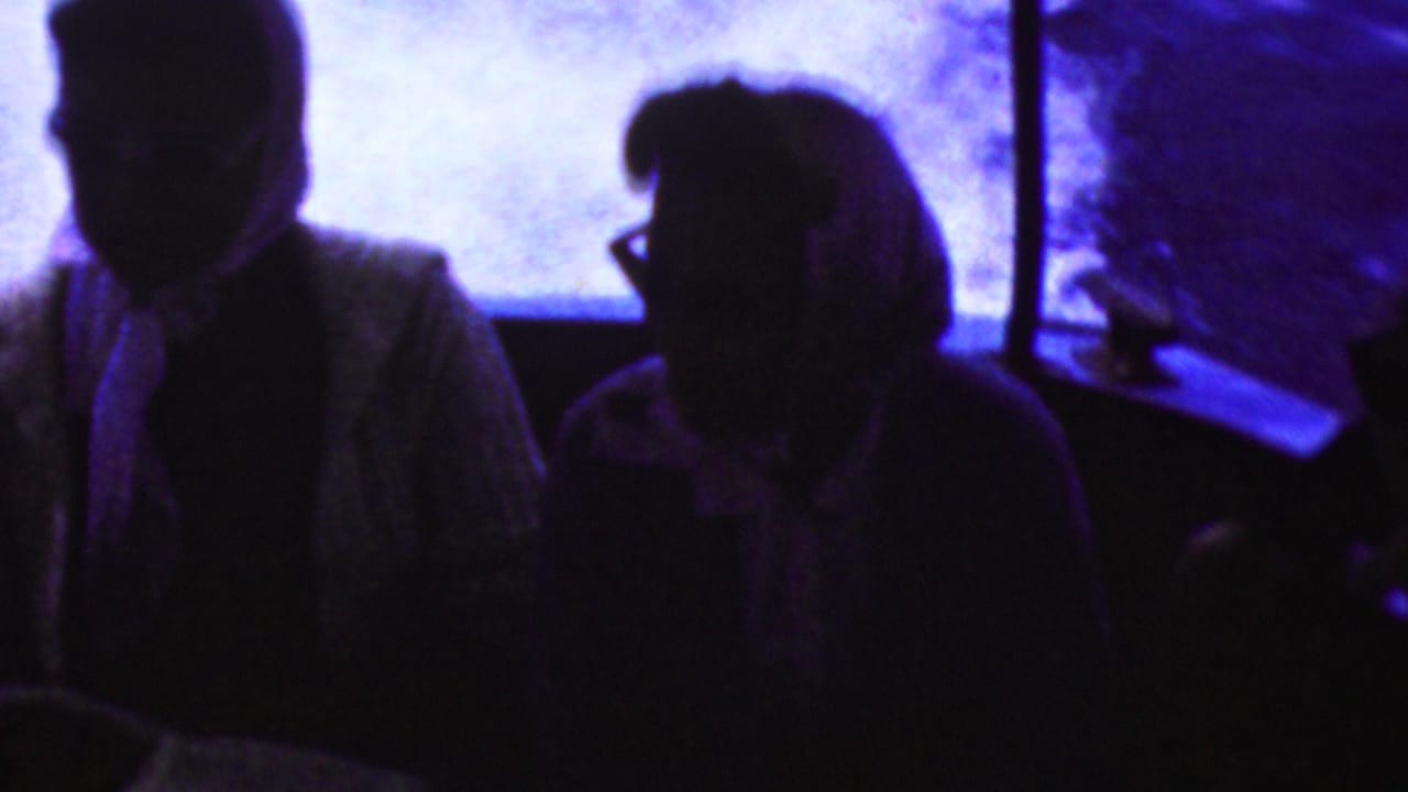 Silhouetted passengers sit inside a boat during a 1961 California home-movie scene, with intense purple-blue light and water reflections behind them.