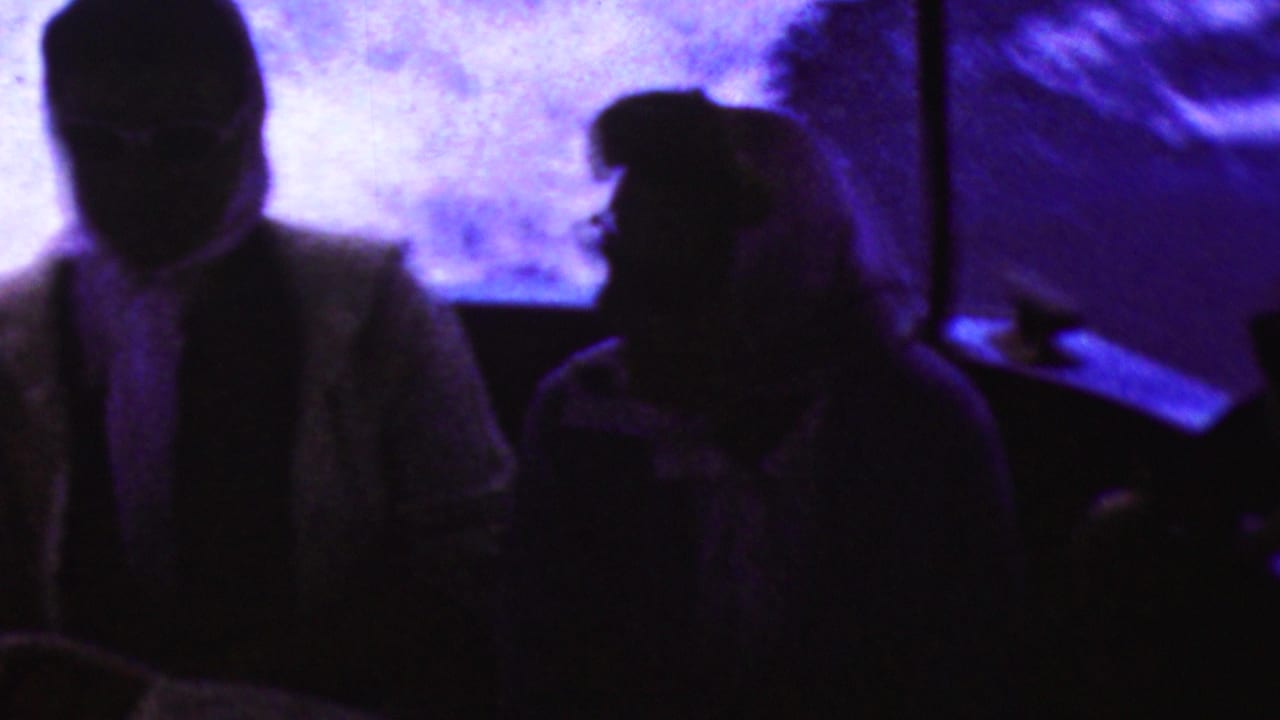 Two adult passengers appear in silhouette inside the boat, backed by bright purple-blue reflected light in this 1961 California 8mm frame.