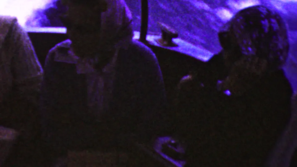 Several passengers are partly visible in a dim boat interior, with purple-blue light and soft 8mm grain obscuring facial detail.