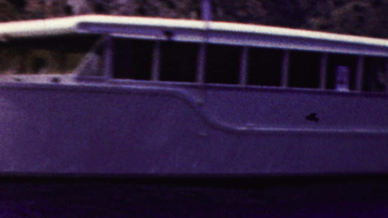 Side of a white cabin motorboat with long dark windows on the water.