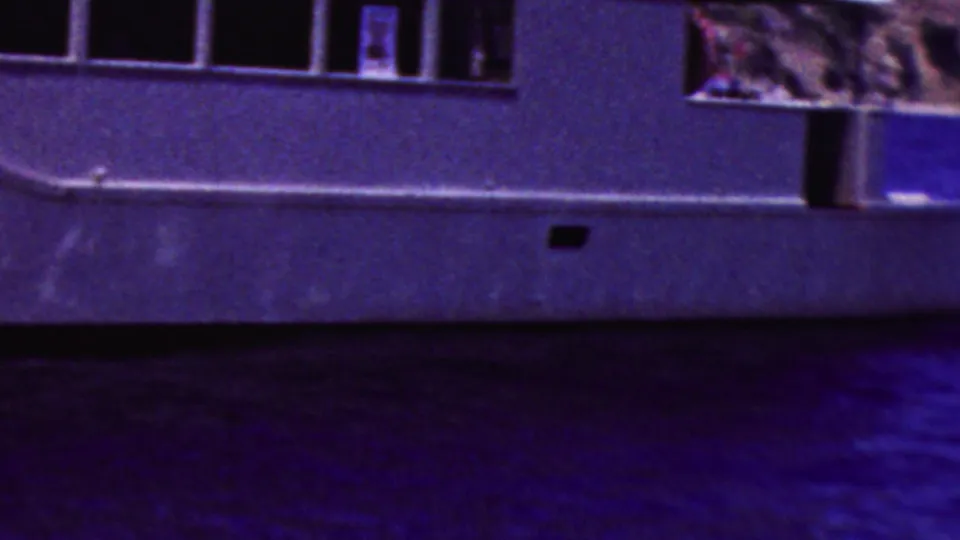 1961 California 8mm frame focused on the midsection of the white motorboat, with dark cabin windows, hull fittings, and coastal water beneath.